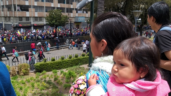 아기를 업은 에콰도르 선주민 여성이 시위 현장을 바라보고 있다. ©BBC