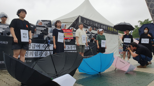 기자회견 참가자들이 '실업급여'라고 적힌 우산을 빼앗긴 채 비를 맞고 서 있는 퍼포먼스를 진행하고 있다. ⓒ이수진 기자