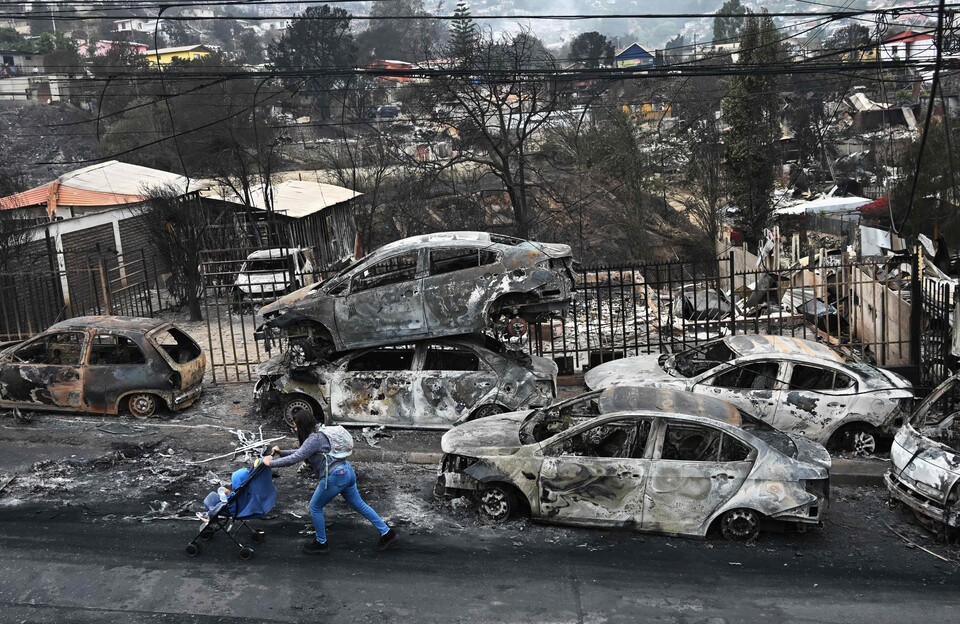 (킬푸에 AFP=연합뉴스) 4일(현지시각) 칠레 킬푸에 지역 한 마을에서 주민이 불에 타버린 승용차 옆 도로를 지나가고 있다.