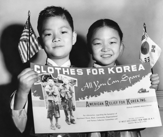 아메리칸 릴리프 퍼 코리아(ARK)가 1953년 옷 수집 캠페인을 위해 만든 포스터를 들고 있는 그레이스 김(오른쪽)-존 김 남매. ARK는 전쟁 구호민을 위한 이 캠페인을 위해 포스터 2만5000개를 제작했다. ‘뉴욕 타임스’ 53년 3월17일치에 실린 사진. ⓒ뉴욕타임스