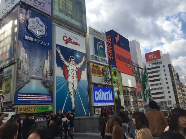 오사카 도톤보리에 다양한 광고판들 사이에 있는 글리코상. 인증삿의 배경으로 사람들이 사진을 찍는다. ⓒ장병인